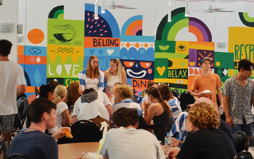 Students in a cafeteria with a colorful mural promoting school values like respect and belonging.